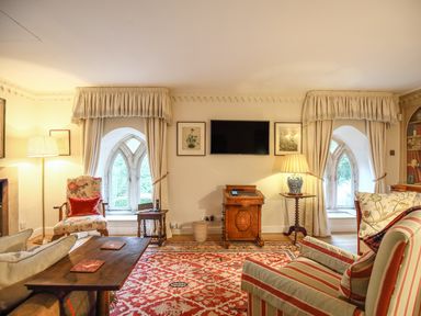 A living room with floral and striped armchairs a wooden coffee table a patterned rug and a wall-mounted TV at All Souls Cottage in Eastleach Cotswolds