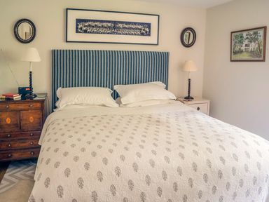 A bedroom with a bed with a striped headboard bedside tables with lamps and framed pictures on the walls at All Souls Cottage in Eastleach Cotswolds