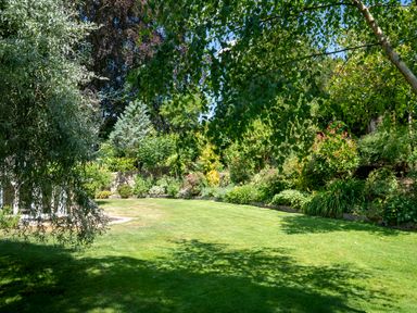 A garden with grass lawn surrounded by trees and shrubs at All Souls Cottage in Eastleach Cotswolds