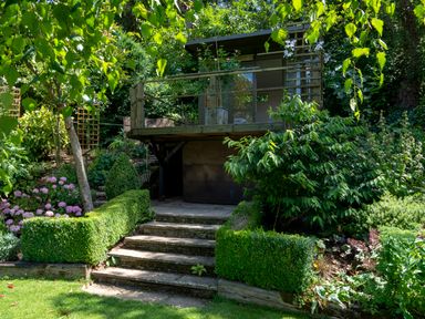 A garden with stone steps leading to a raised wooden deck surrounded by plants at All Souls Cottage in Eastleach Cotswolds
