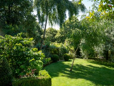 A garden with a lawn trees and bushes at All Souls Cottage in Eastleach Cotswolds