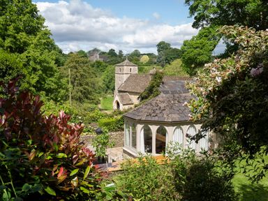 A garden with a gazebo and a stone church building surrounded by trees at All Souls Cottage Eastleach Cotswolds