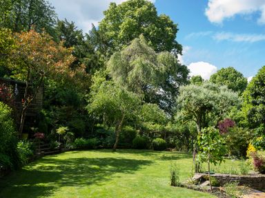 A garden with trees bushes and a lawn at All Souls Cottage Eastleach Cotswolds