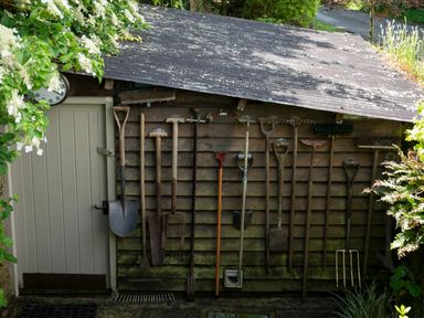 A garden shed with gardening tools hanging on the wall including rakes shovels hoes and forks at All Souls Cottage in Eastleach Cotswolds