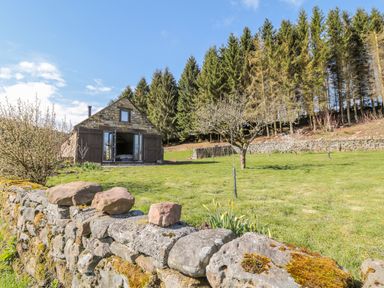 A stone barn with open wooden doors in a grassy yard with trees and a stone wall at Thompson Rigg Barn in Langdale End near Thornton Dale