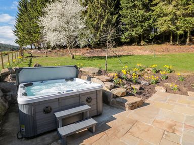 An outdoor hot tub with steps next to a garden with flowers and trees at Thompson Rigg Barn in Langdale End near Thornton Dale