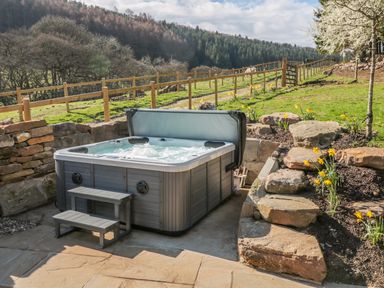 An outdoor hot tub with steps on a stone patio surrounded by stone walls and flowers at Thompson Rigg Barn Langdale End near Thornton Dale