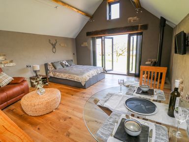 A bedroom with a bed a leather armchair a wicker ottoman a dining table and glass doors at Thompson Rigg Barn Langdale End near Thornton Dale