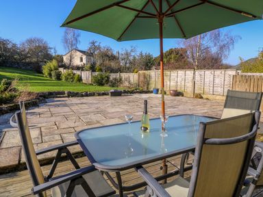A patio table with two glasses and a bottle under an umbrella in a garden at Langtree Arnside