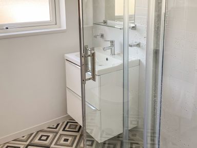 A bathroom with a white sink cabinet a glass shower door and a window with frosted glass at Ty Gilbert in Benllech