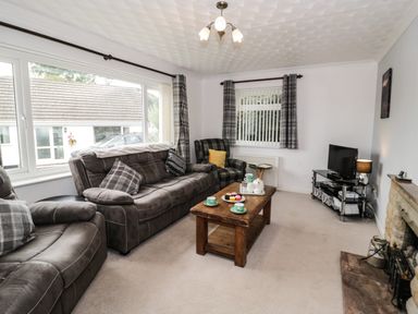 A living room with sofas a wooden coffee table a television and a fireplace at Ty Gilbert in Benllech