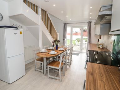 A kitchen dining area with a wooden table set for six and a staircase along the wall at Ty Gilbert in Benllech