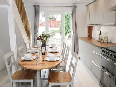 A kitchen dining area with a wooden table set with dishes and wine in front of glass doors at Ty Gilbert in Benllech