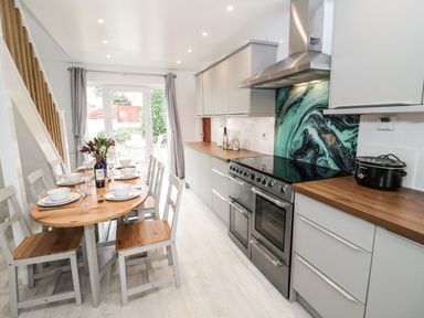 A kitchen and dining area with a wooden table set for six and white chairs at Ty Gilbert in Benllech