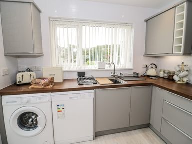 A kitchen with a washing machine dishwasher sink and cabinets at Ty Gilbert in Benllech