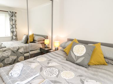 A bedroom with a bed with patterned bedding and pillows beside a nightstand with a lamp and mirrored closet doors at Ty Gilbert in Benllech