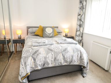 A bedroom with a double bed covered with patterned bedding and pillows two bedside tables with lamps and mirrored wardrobe at Ty Gilbert in Benllech