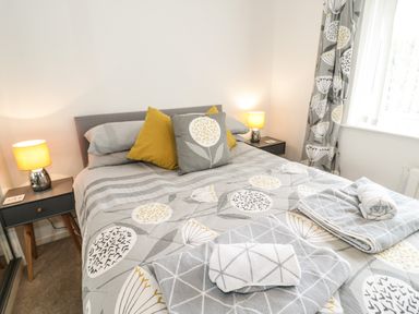 A bedroom with a double bed two bedside tables with lamps patterned bedding and folded towels on the bed at Ty Gilbert in Benllech