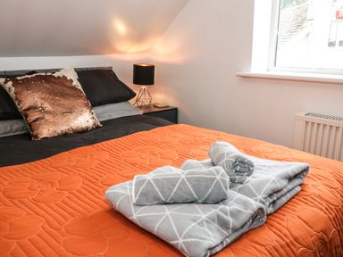 A bedroom with a bed covered with an orange quilt and gray towels near a window at Ty Gilbert in Benllech