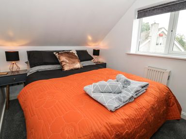 A bedroom with a bed with an orange quilt and two gray towels on top two bedside tables with black lamps and a window at Ty Gilbert in Benllech