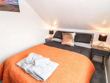A bedroom with a bed covered by an orange quilt and gray towels placed on top at Ty Gilbert in Benllech