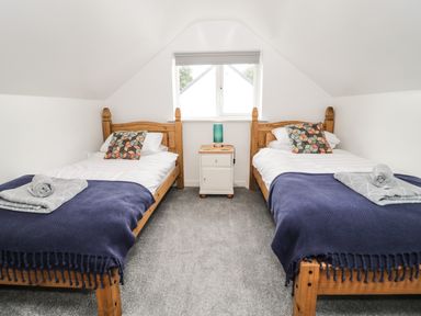 A bedroom with two single wooden beds a nightstand with a lamp and a window at Ty Gilbert in Benllech