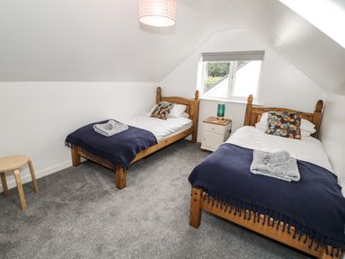 A bedroom with two single wooden beds a bedside table a window and a small stool at Ty Gilbert in Benllech
