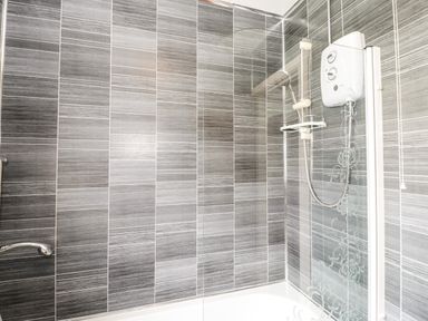A bathroom with a shower, water heater, and grey tiled walls at Ty Gilbert in Benllech