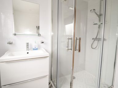 A bathroom with a sink and mirror next to a glass door shower at Ty Gilbert in Benllech