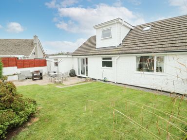 A backyard with a lawn patio furniture and a white house with windows and a dormer at Ty Gilbert in Benllech