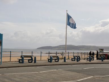 A seaside promenade with benches and a blue flag by the beach at Ty Gilbert in Benllech