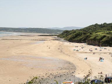 A wide sandy beach with people and tents near grassy cliffs at Ty Gilbert in Benllech