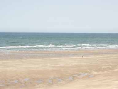 A sandy beach with small pools of water and people walking near the ocean at Ty Gilbert in Benllech