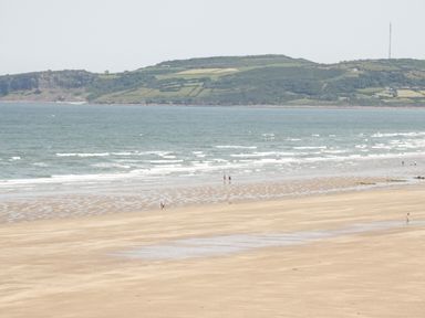 A wide sandy beach with a few people walking near the water and hills in the background at Ty Gilbert in Benllech