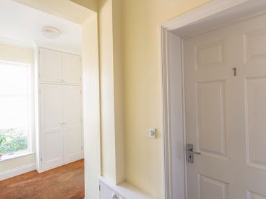 A hallway with a white door numbered 7 and built in white cupboards near a window at 1 Lyndhurst in Salcombe