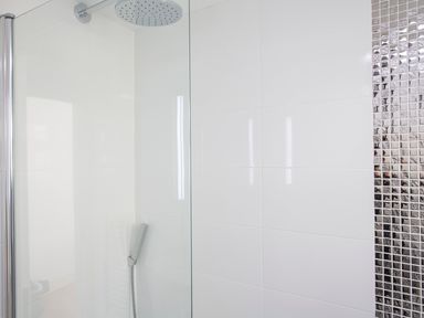 A shower area with a round showerhead and a handheld shower on white tiled walls with a section of small square mosaic tiles at 1 Lyndhurst in Salcombe