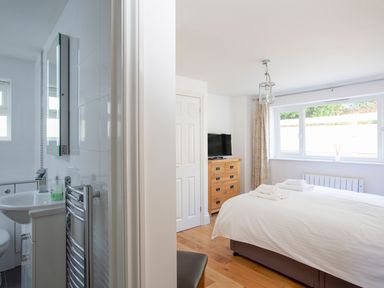 A bedroom with a bed and folded towels next to a window and a bathroom with a sink and mirror at 1 Lyndhurst in Salcombe
