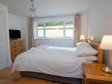 A bedroom with a double bed white bedding wooden furniture and windows with curtains at 1 Lyndhurst in Salcombe