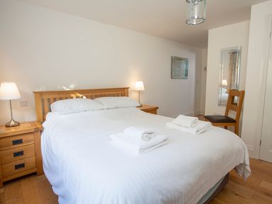 A bedroom with a double bed white bedding two bedside tables with lamps a wooden chair and mirrors at 1 Lyndhurst in Salcombe