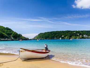 A small boat on a sandy beach with clear water and green hills in the background at 1 Lyndhurst in Salcombe