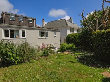 A garden with green grass and flowering plants beside two white houses at 1 Lyndhurst in Salcombe