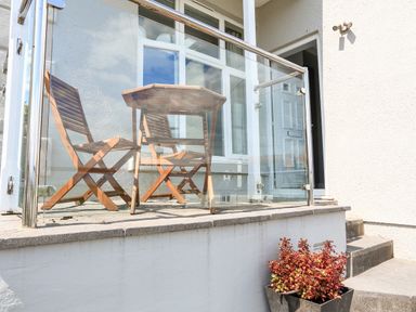 A small outdoor patio with two wooden chairs a table glass railing potted plant and a door at 1 Lyndhurst in Salcombe