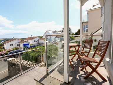 A balcony with wooden chairs and a small table overlooking houses and a road at 1 Lyndhurst in Salcombe