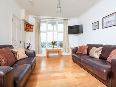 A living room with two leather sofas facing each other a wooden table with flowers in front of a window and a wall-mounted TV at 1 Lyndhurst in Salcombe