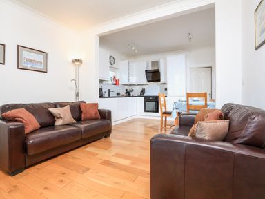 An open living room and kitchen area with two brown leather sofas and a dining table at 1 Lyndhurst in Salcombe