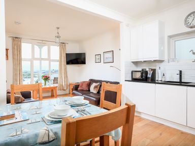 A dining table set with bowls and utensils in a kitchen living room with a sofa TV and large window at 1 Lyndhurst in Salcombe