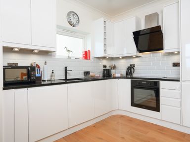 A kitchen with white cabinets black countertop a microwave oven electric kettle and cooking utensils at 1 Lyndhurst in Salcombe