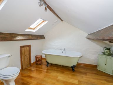 A bathroom with a bathtub toilet wooden stool small door and cabinet under slanted ceiling with skylight at Rose Cottage in Lowick Bridge