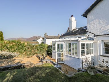 A garden with grass and gravel next to a white house with a glass porch at Rose Cottage in Lowick Bridge