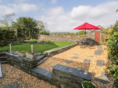 A garden with a stone wall a grass area and a seating area with a red umbrella at Rose Cottage in Lowick Bridge